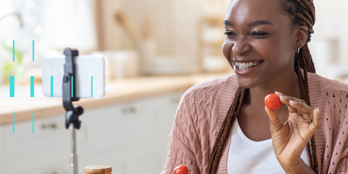 Mulher sorrindo, segurando um tomate, olhando para tela de celular