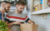 Dois homens em uma cozinha, olhando as compras de alimentos que fizeram