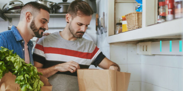 Dois homens em uma cozinha, olhando as compras de alimentos que fizeram