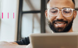 Homem de óculos, sorrindo, e mexendo em tablet