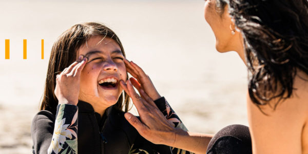 Mulher passando protetor solar no rosto de sua filha, que está sorrindo